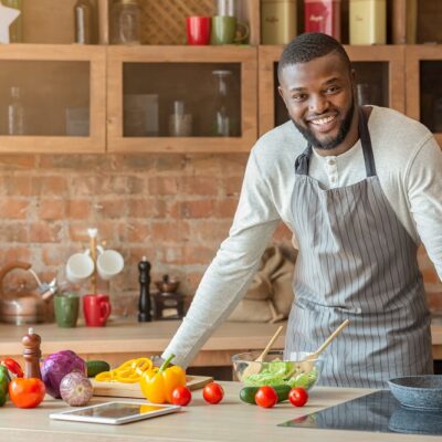 Attractive black positive man posing at kitchen while cooking dinner for his family, free space
